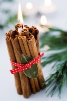 Décoration de Noël simple avec un paquet de bâtons de cannelle attachés autour d'une bougie avec un ruban rouge et une feuille de laurier