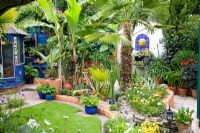 Petit jardin tropical de style marocain avec Trachycarpus fortunei et Agave en parterre surélevé mixte