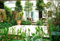 De cet appartement de jardin meublé vert pâle, des portes coulissantes s'ouvrent sur une cour intérieure. L'espace est divisé par des charmes blanchis et des planches de vivaces délicates et comprenant un étang en forme de stip.