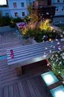 Terrasse en terrasse la nuit avec éclairage led rose et blanc et banc en bois avec bougies, parterres surélevés avec Stipa et Gaura - Roof garden, Holland Park, Londres