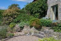 Jardin en gravier et mur en pierre planté avec des marches menant à un coin salon et à des portes-fenêtres