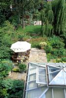Conservatoire qui s'ouvre sur une terrasse pavée en pierre, offrant un coin repas extérieur, bordé d'une plantation douce - Islington, Londres