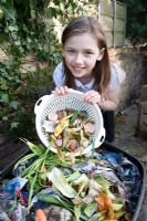Fille vidant une passoire en plastique avec des déchets alimentaires dans le bac à compost