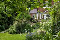Regardant le jardin vers la maison encadrée par les feuilles Liriodendron tulipifera, courbant la pelouse et les parterres de fleurs - Eldenhurst