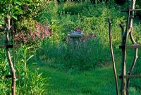 Chemin d'herbe fauchée entourant un vieux cadran solaire dans une petite parcelle de fleurs sauvages, y compris le stock parfumé de nuit