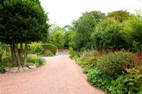 Jardin avant d'une grande maison individuelle avec allée de gravier rouge et buissons de houx