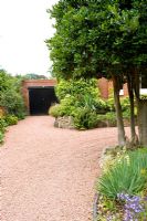 Jardin avant d'une grande maison individuelle avec allée de gravier rouge et buissons de houx