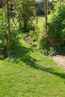 Chemin herbeux menant de la pelouse à travers le treillis incurvé soutenant les rosiers grimpants et les clématites - Bridge House, NGS garden, Lancashire
