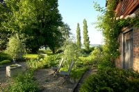 Patio en gravier, avec deux chaises en bois donnant sur le jardin et la campagne de l'East Sussex, tôt le matin