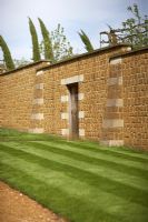 Entrée latérale des jardins de Broughton Grange. Pelouse avec des bandes de tonte et des sommets de cyprès italiens montrant sur le mur. Avril.