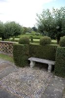 Siège en pierre et motif de galets en voie devant Buxus - Boîte coupée dans le jardin Est à Hatfield House.