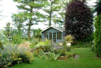 Pelouse menant à une maison d'été isolée et à une rocaille avec des conifères matures. Fagus sylvatica 'Purpurea' - Hêtres cuivrés au-delà. Crabtree Lane, NGS garden Lancashire