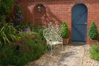 Porte de jardin en bois dans le mur de briques. Dalle de pierre et chemin de gravier avec chaise en fil de fer. 'Hazelwood '. Jacqueline Iddon Hardy Plants, jardin NGS, Lancashire