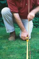 Guide étape par étape pour mesurer un jardin. Utilisez une canne pour marquer des points spécifiques le long de la ligne mesurée.