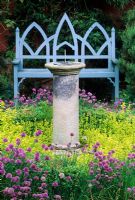 Siège en bois de style gothique bleu et cadran solaire en pierre entouré d'Origanum vulgare 'Aureum' et Allium - Ciboulette