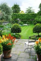 Vue de la terrasse et du jardin au printemps, siège de jardin pliant vintage, pots de fleurs murales, vue sur la pelouse avec boîte topiaire