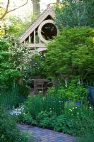 Un chemin de briques mène à travers le jardin vers un pavillon d'été en chêne vert. Leur