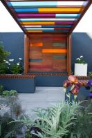 Une pergola en bois avec des panneaux de verre colorés et un coin salon. Jardin de l'Université de Worcester, médaillé d'argent doré, RHS Chelsea Flower Show 2010