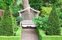 Siège au fond du jardin arrière avec Buxus bas - Haie de buis et Pyramides de Taxus - If. Mathern House, Mathern, Monmouthshire, Pays de Galles. Début juin. Ouverture du jardin pour le programme des jardins nationaux.
