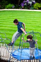 Oliver et Rueben (petits-enfants du propriétaire) sur un cadre d'escalade dans une aire de jeux dans le jardin arrière. Mathern House, Mathern, Monmouthshire, Pays de Galles. Début juin. Ouverture du jardin pour le programme des jardins nationaux.