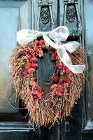 Couronne d'automne de pommes de pin et de baies, attachée avec un ruban blanc, suspendue à un heurtoir de porte en fonte