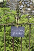 Panneau en ardoise sur le portail en fer forgé, indiquant 'Je ' m dans le jardin'