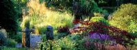 Un chemin de gravier mène à travers des vivaces, des herbes, des arbustes et des arbres dans le jardin à Pinsla Lodge, Cornwall