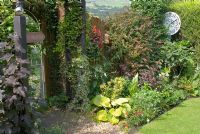 Coin d'un petit jardin arrière avec des plantations mixtes comprenant Rhododendron, Buddleia, Hosta, Hedera, Begonia et Clematis et une clôture lambrissée en bois avec porte ornée et caractéristiques - cadran d'horloge fabriqué à partir d'un plateau et d'un panneau peints. 'Trevinia', Stubbins, Lancashire NGS