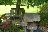 Banc circulaire sous arbre et champignons ornementaux en bois. Parsons Cottage, Essex, Royaume-Uni