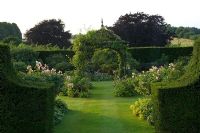 Jardin de campagne avec Taxus - Haies d'ifs et chemin d'herbe menant au gazebo avec escalade Rosa - Roses. Jardin Robinson, Ousden House, Suffolk