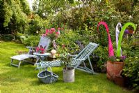 Chaises longues sur la pelouse à côté de parterre de fleurs avec Rosa et ornement coloré fait de bandes de tissu en pot en terre cuite