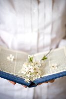 Femme portant une chemise blanche, tenant un livre ouvert avec des fleurs