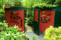 Le jardin des trois amis de l'hiver a une prune à fleurs d'hiver, Prunus mume, en son centre et Sasa veitchii - Bamboo. Phénix sculpté à la main et porte de flanc de dragon dans le jardin du mur rouge. Beggars Knoll, Newtown, Westbury, Wiltshire, Royaume-Uni