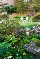 Le parterre de fleurs devant la maison comprend des azalées, des rhododendrons, des hellébores, des épimédiums et des alpins dans un creux de pierre, avec une pelouse au-delà. Chiffchaffs, nr Bourton, Dorset, Royaume-Uni