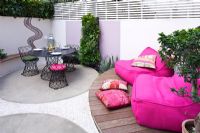 Petit jardin patio avec terrasse en bois surélevée avec chaises roses, coin repas et mosaïque par Celia Gregory, Londres.