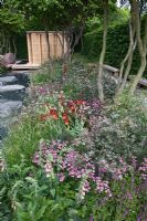 Un parterre de plantes naturalistes de plantes vivaces et d'herbes à côté d'un long canal d'eau mène à un pavillon japonais