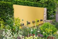 Parterres d'été colorés soutenus par Taxus - couverture en if et mur de caractéristiques peint en jaune avec des tuyaux d'eau. 'The Daily Telegraph Garden', médaillé d'or et Best in Show - RHS Chelsea Flower Show 2011