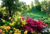 Les rives colorées des azalées bordent un côté du ruisseau, avec des pâturages ouverts parsemés d'arbres matures s'élève de l'autre côté - Minterne, Minterne Magna, Dorset, UK