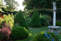 Le jardin cadran solaire avec le soleil de fin d'après-midi éclairant les fougères arborescentes, les pics coniques et les plantes herbacées exotiques, y compris les Salvias, les Dahlias et les Ricinus - Exbury Gardens, Exbury, Hants, UK