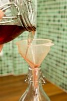 Faire du Sloe Gin fait maison - verser du liquide à travers l'entonnoir dans une bouteille en verre