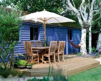 Pavillon bleu avec terrasse en bois, table, chaises et parasol, bouleaux et hamac