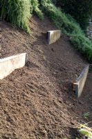 Méthode de stabilisation et de terrassement d'un talus escarpé par des pièces épaisses de bois traité émaillées fixées par un angle métallique.