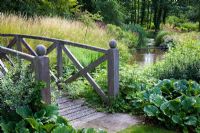 Pont de style Monet traversant le ruisseau avec feuillage et herbes de Bergenia