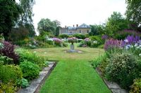 Les parterres de faucille, dans le jardin à l'ouest de la maison, avec une urne centrale et des parterres pleins de Phlox, Lythrums, Crinums et autres plantes vivaces herbacées - Old Rectory, Pulham, Dorset