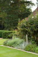 Bâtiment de jardin en toit de briques et de tuiles avec parterre de fleurs bordé par un chemin de dalle de pavage. Les plantes comprennent - Lavandula et Stachys byzantina - Mannington Hall, Norfolk, Royaume-Uni