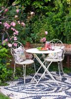 Patio avec sol en mosaïque de galets, table et chaises en métal blanc avec coussins