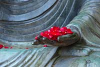 Pétales de rose rouge sur une grande main de Bouddha de jardin