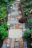 Chemin de style jardin de chalet fait de matériaux récupérés, y compris des dalles, des briques, des pavés en blocs de béton et des cailloux
