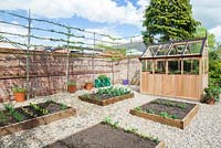 Pas à pas - Vue d'ensemble du potager avec bordures de légumes surélevées et serre au début de l'été