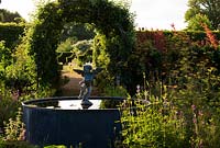 Fontaine en plomb avec putto et dauphin au centre de la cuisine biologique et du jardin de fleurs, avec des tunnels de pommes ombrageant les sentiers voisins.